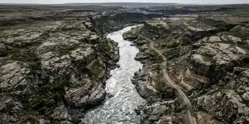 A bird's-eye view of a turbulent river cutting through a fractured, evolving landscape under an overcast sky, symbolizing rapid cultural shifts and societal changes.